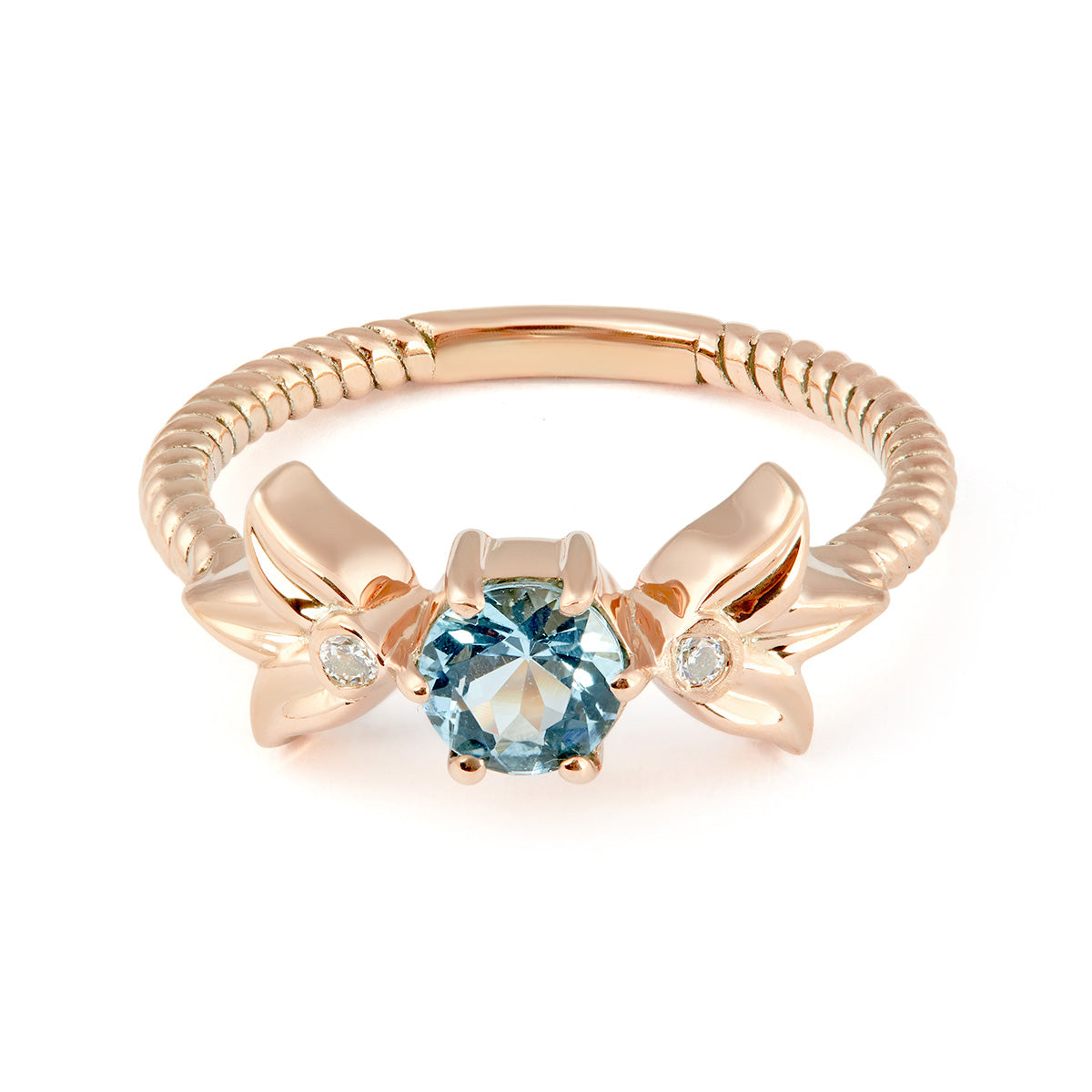 A rose gold ring featuring a central round-cut aquamarine secured by six prongs. The band is flanked by two rose gold floral motifs, each accented with a small, inset clear diamond.