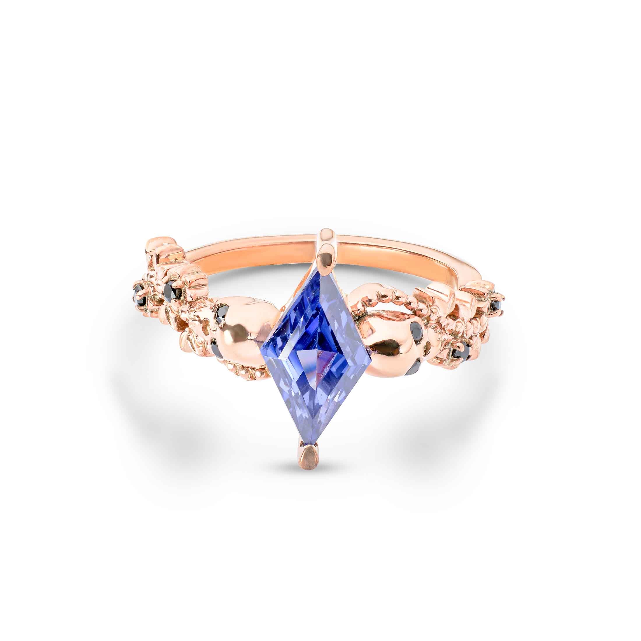 Rose gold ring with a kite-cut purple gemstone flanked by two polished gold skulls.