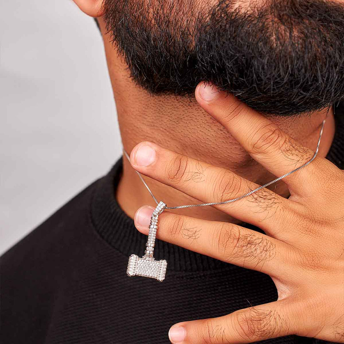 Silver pendant shaped like a hammer with clear stones on a dark background