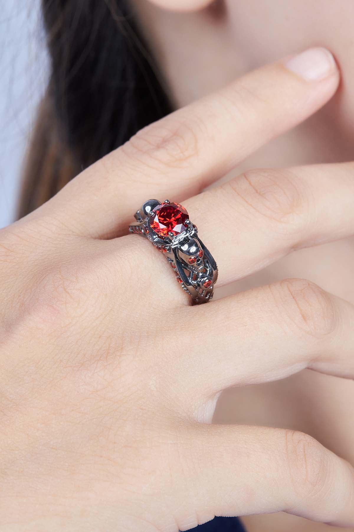 Close-up of a woman's hand wearing a skull ring with red garnet gemstone.