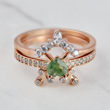 Rose gold ring with green gemstone and diamonds on a light background