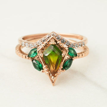 Rose gold ring with green gemstones on a white background