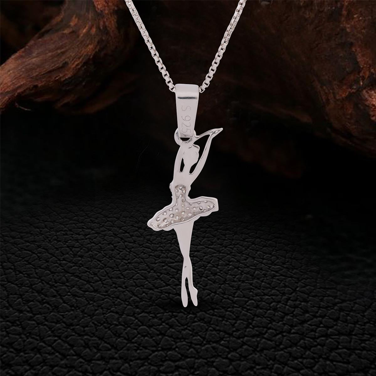 Backside of Silver ballerina pendant on a chain against a dark textured background