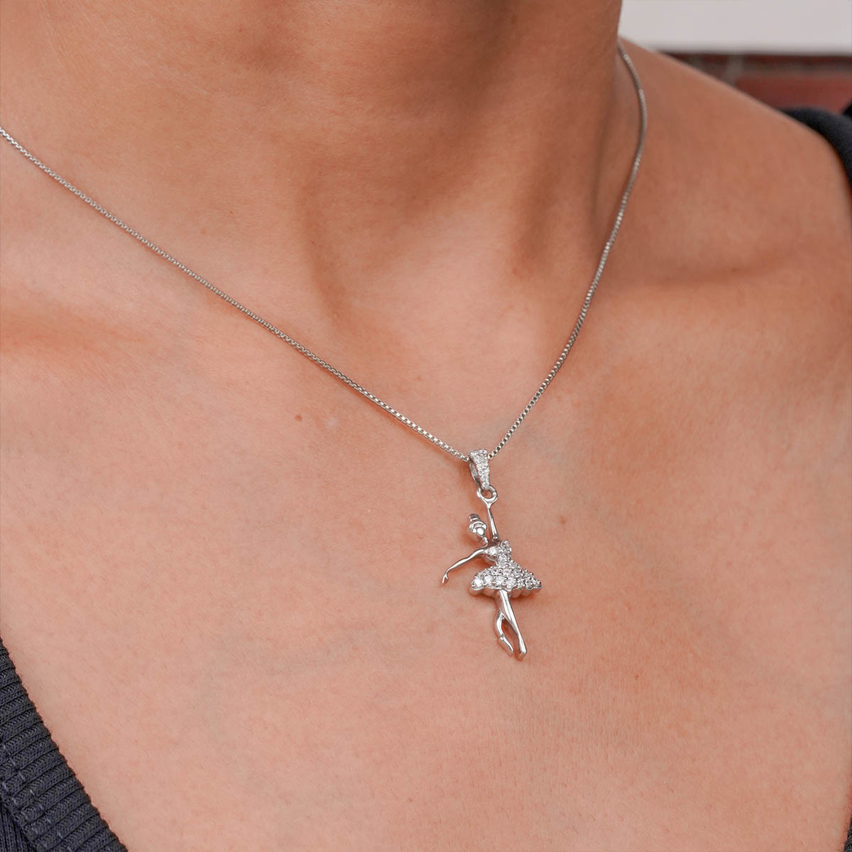 Silver necklace with a ballerina pendant on a person's neck