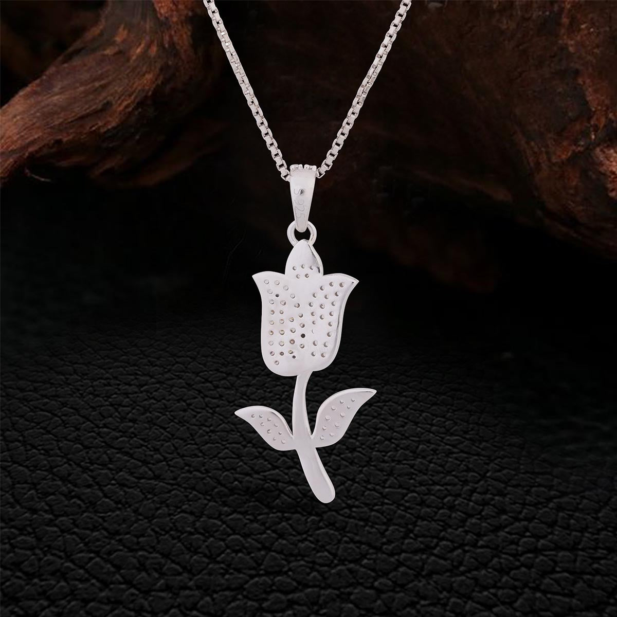 Backside of Silver tulip-shaped pendant on a chain against a dark textured background