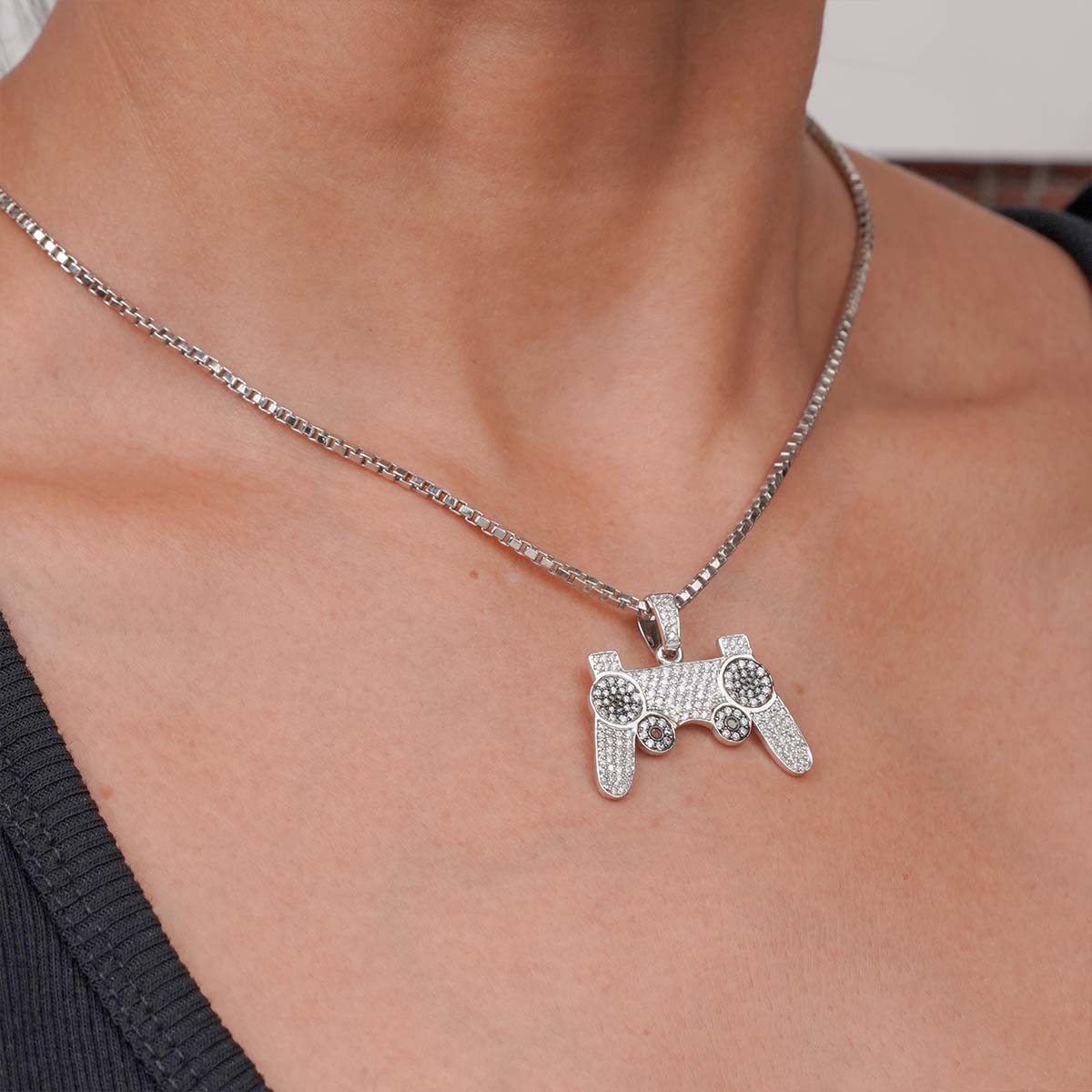 Silver pendant shaped like a gaming controller on a necklace, worn by a person.