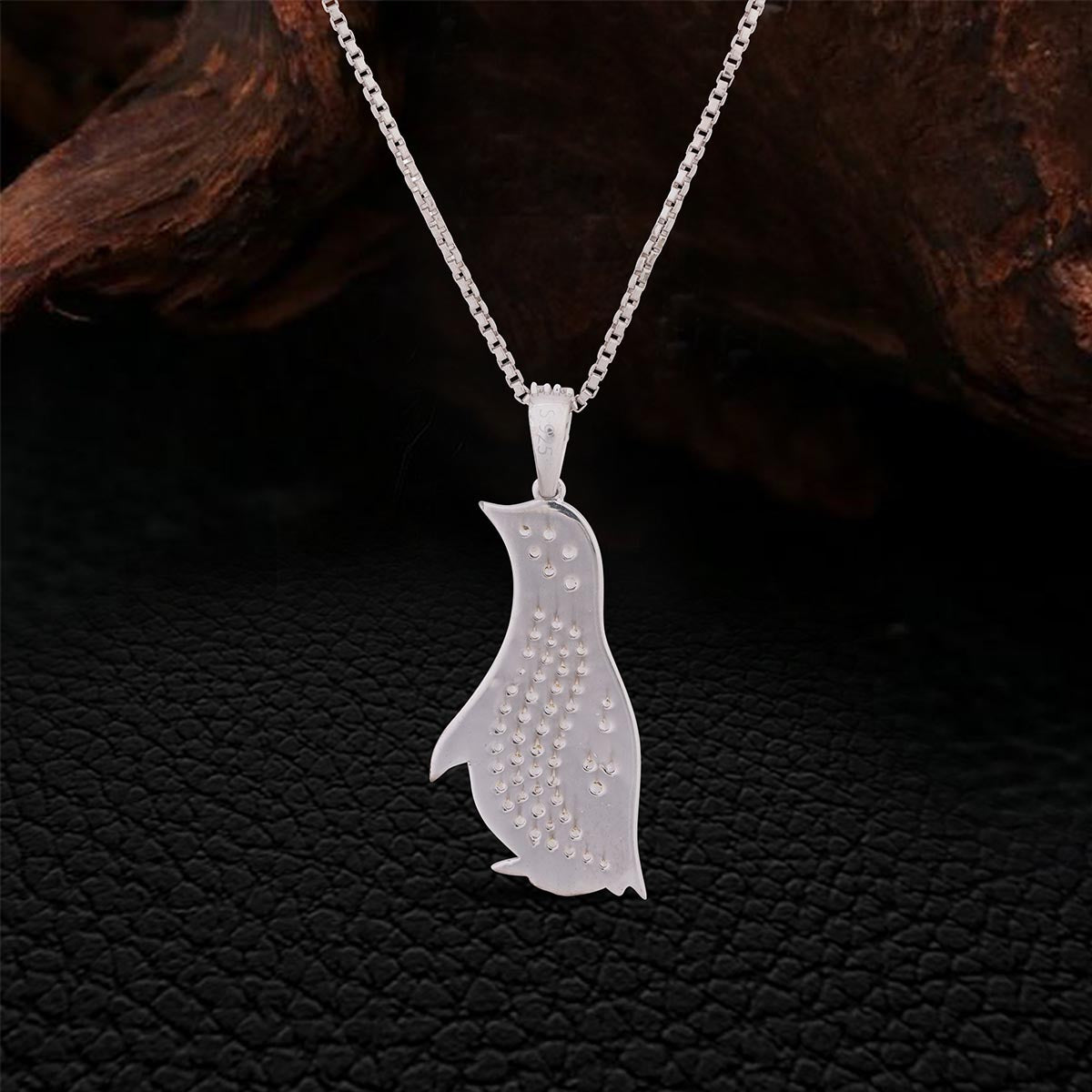 Backside of Silver penguin pendant necklace on a dark textured background