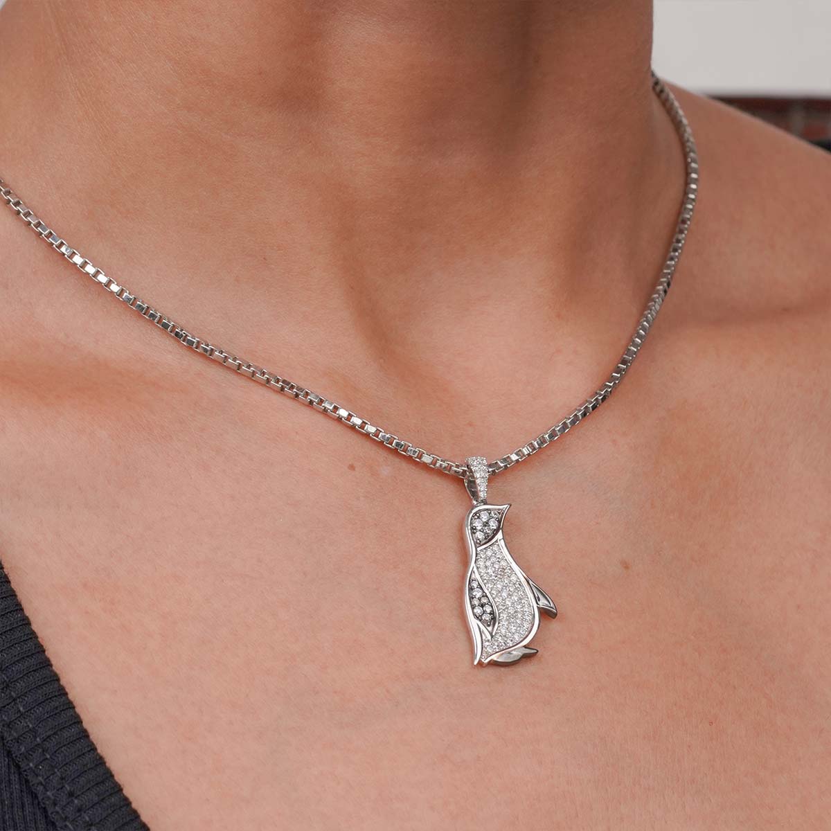 Silver necklace with a penguin pendant on a person's neck