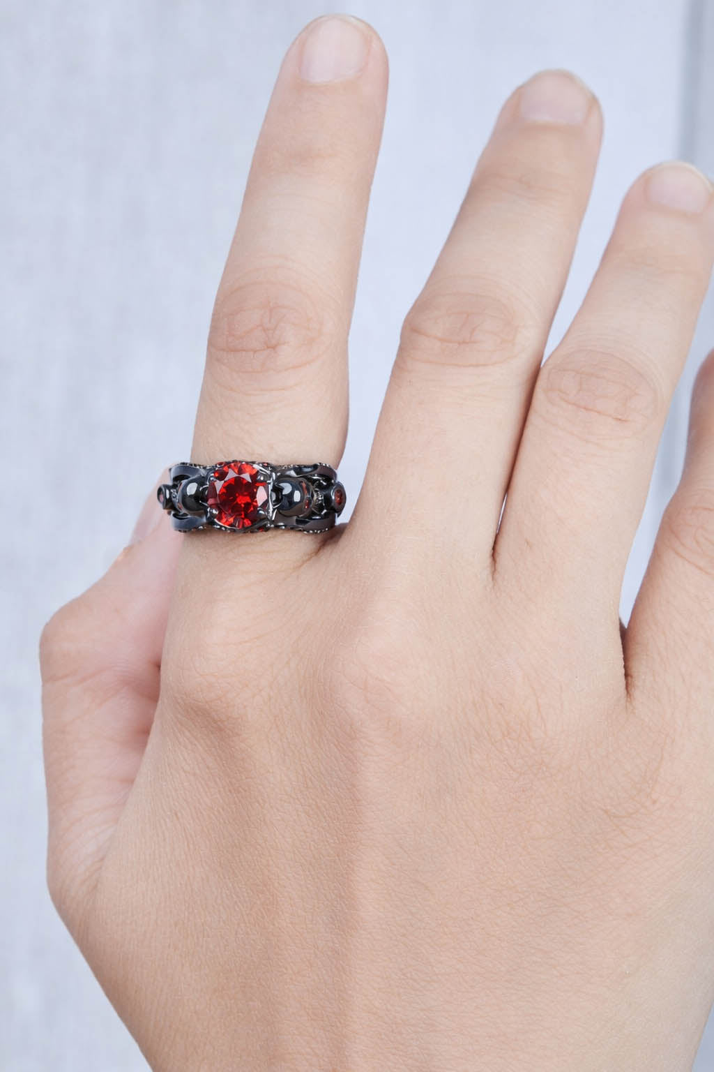 Hand wearing a black skull ring with red gemstones