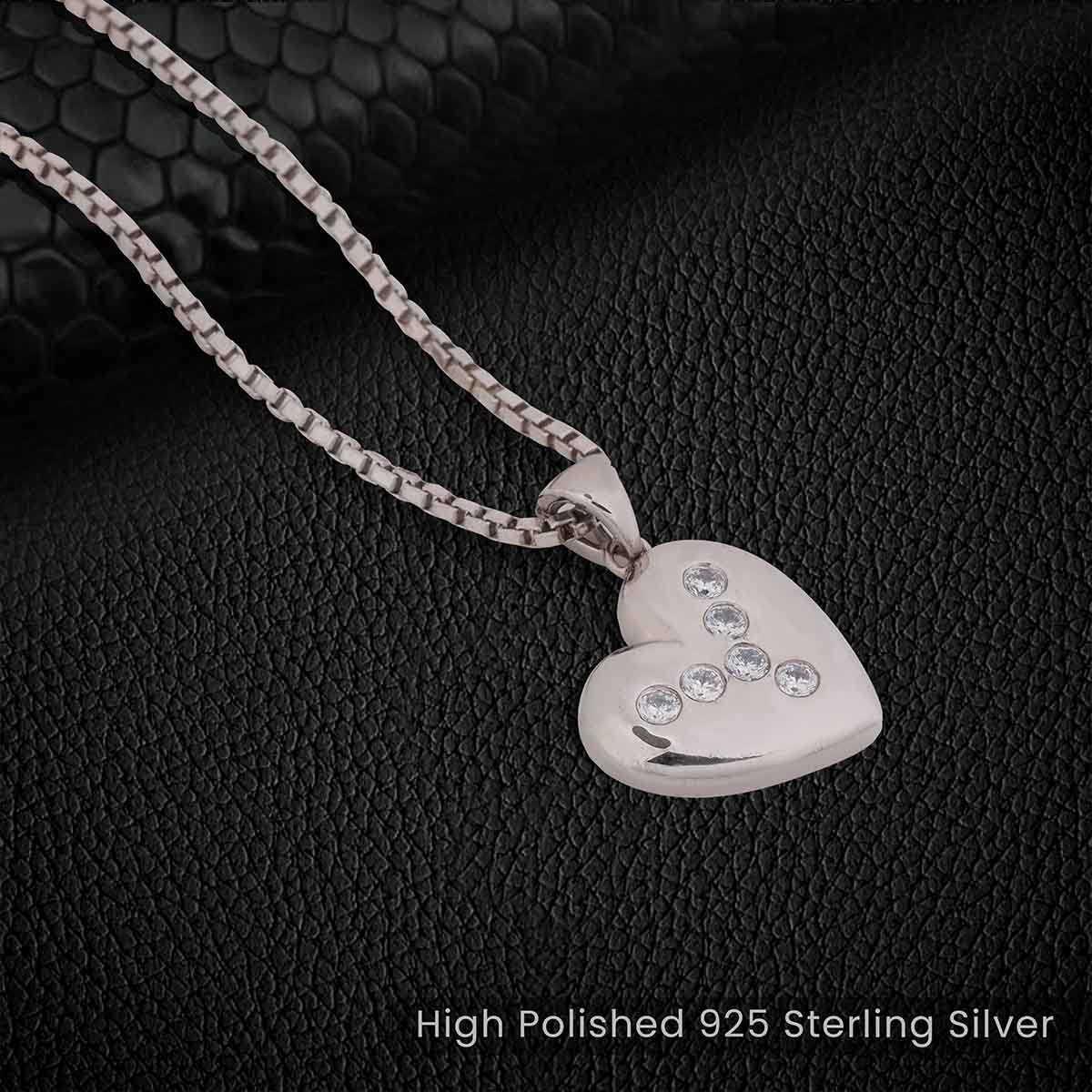 Silver heart-shaped pendant with embedded stones on a black textured background