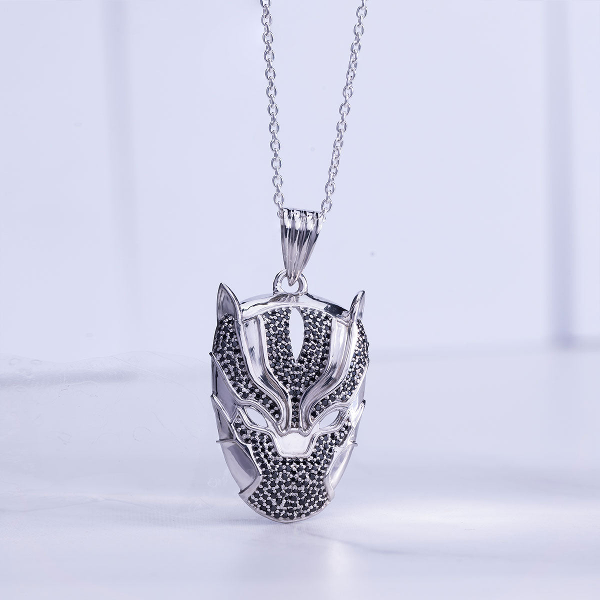 Silver pendant shaped like a panther face on a chain against a light gray background