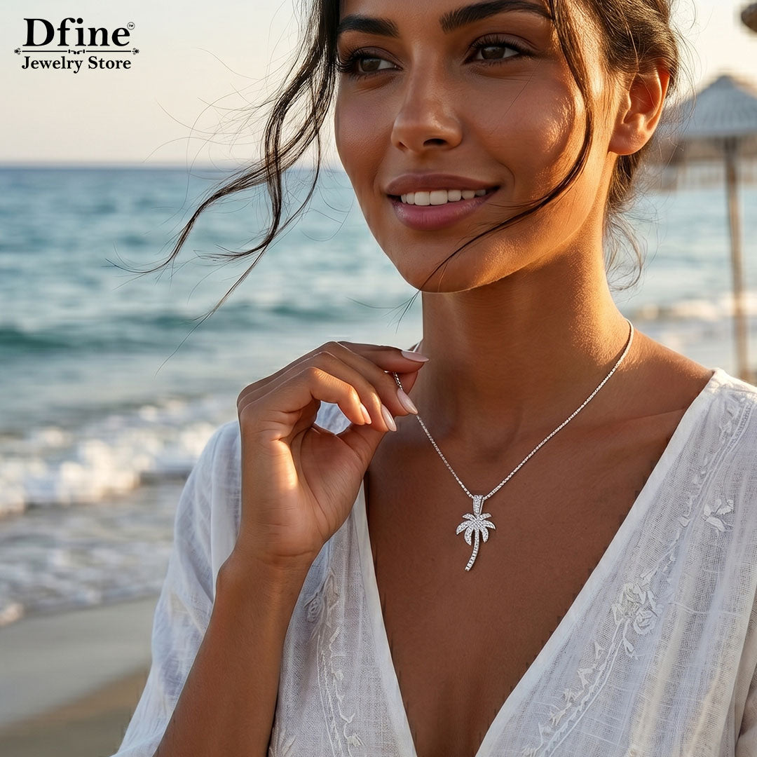 Woman on a beach wearing a silver palm tree necklace with 'Dfine Jewelry Store' branding.